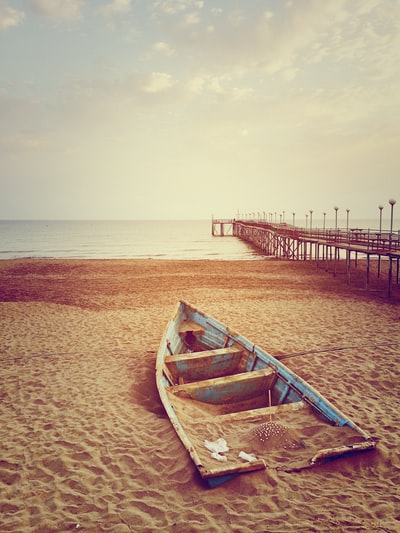 白天，蓝色独木舟在棕色的沙滩上，靠近棕色的木质码头和水体